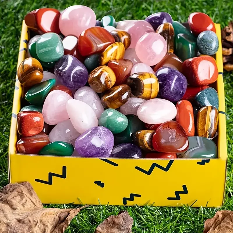 boite-pierres-cristal-polies-multicolores-deco Boîte jaune remplie de pierres de cristal polies multicolores sur un fond d'herbe avec des feuilles sèches