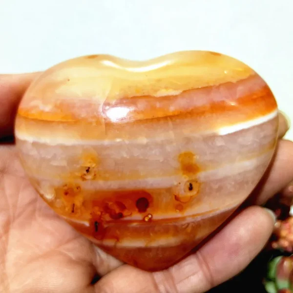 Cœur en agate naturelle avec des bandes blanches et orange, symbole de calme et d'équilibre énergétique, tenu en main