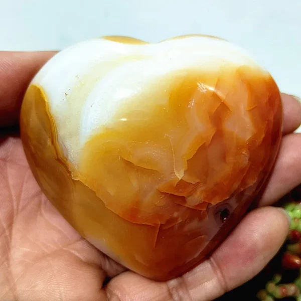 Cœur en agate naturelle avec nuances de blanc et d'orange, symbole de sérénité et d'équilibre, tenu en main