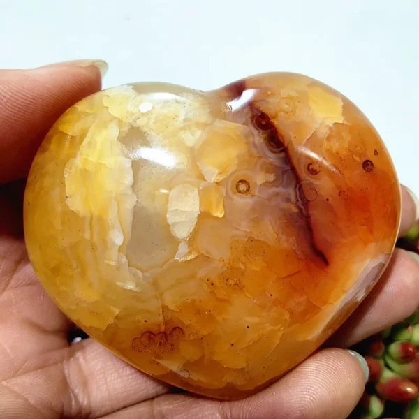 Cœur en agate naturelle avec nuances de jaune et orange, symbole d'énergie et d'équilibre, tenu en main
