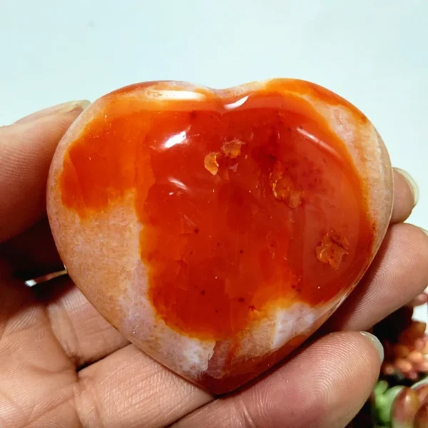 Cœur en agate naturelle aux nuances d'orange vif et de blanc, symbole d'énergie et d'harmonie, tenu en main