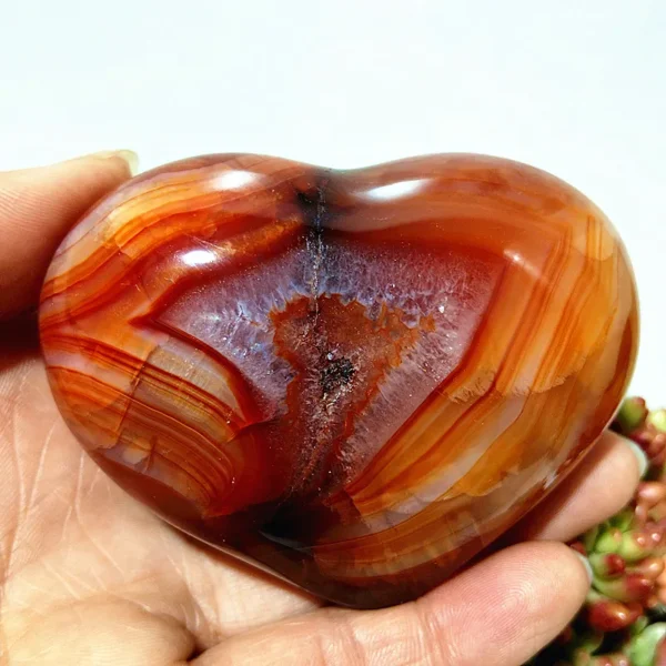 Cœur en agate rouge naturelle avec inclusion cristallisée et motifs de bandes, symbole d'énergie et d'harmonie, tenu en main