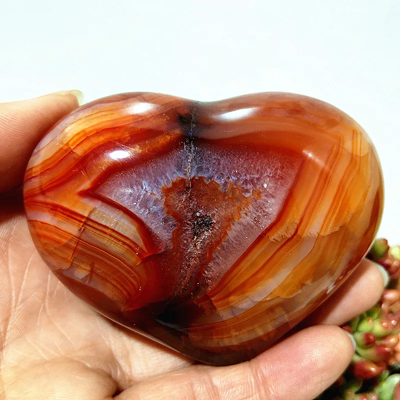coeur-agate-rouge-bandes-cristallise-energie-harmonie Cœur en agate rouge naturelle avec inclusion cristallisée et motifs de bandes, symbole d'énergie et d'harmonie, tenu en main