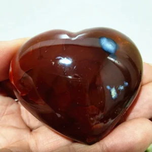 Cœur en agate rouge foncé naturelle avec inclusion bleutée, symbole d'harmonie et d'équilibre, tenu en main