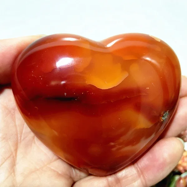 Cœur en agate rouge naturelle, symbole de bien-être et de vitalité, nuances intenses de rouge et orange, tenu en main