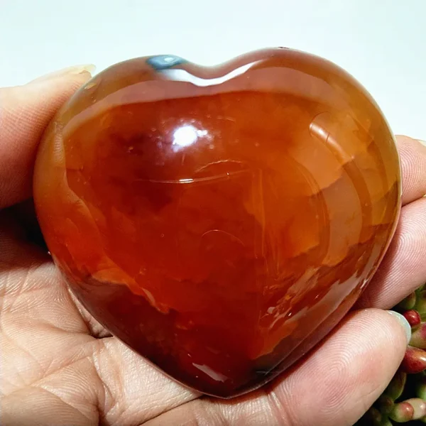 Cœur en agate rouge naturelle, pierre de calme et d'harmonie, nuances chaleureuses de rouge et orange, tenu en main