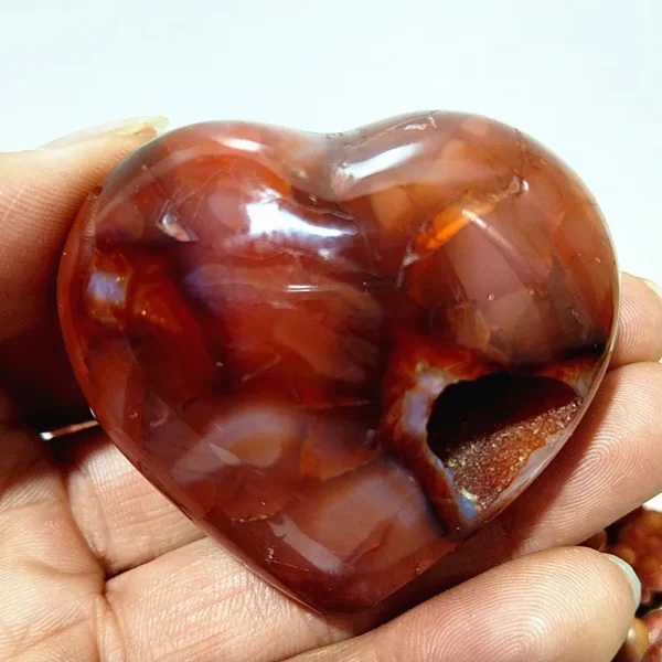 Cœur en agate rouge naturelle avec cavité cristalline, symbole de sérénité et d'équilibre énergétique, tenu en main