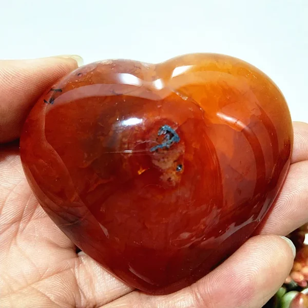 Cœur en agate rouge naturelle avec inclusion, symbole de bien-être et de vitalité, tenu en main