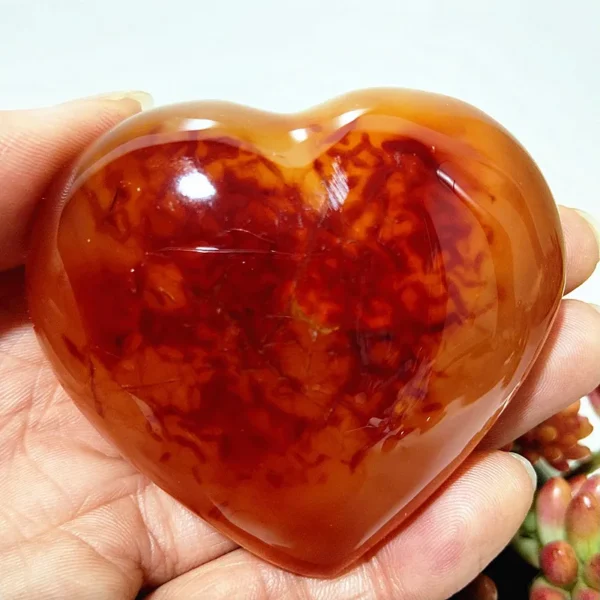 Cœur en agate rouge naturelle avec motifs organiques, symbole de bien-être et d'énergie positive, tenu en main