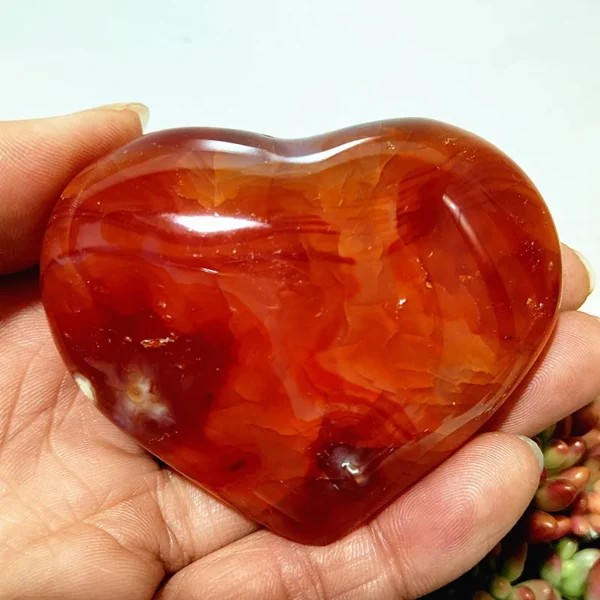 Cœur en agate rouge naturelle, pierre de vitalité et d'harmonie, avec des motifs organiques, tenu en main