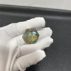 Cristal hexagonal en labradorite naturelle aux reflets bleu et or, tenu par une main gantée.