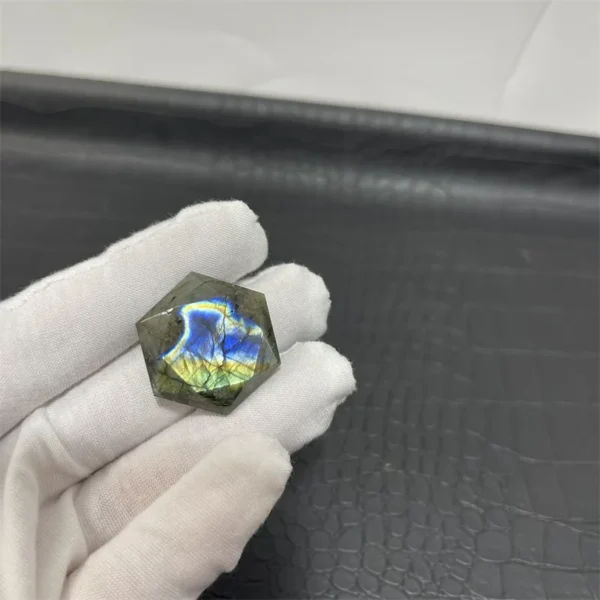 Cristal hexagonal en labradorite naturelle avec des reflets arc-en-ciel, tenu par une main gantée.