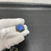 Cristal hexagonal en labradorite naturelle avec des reflets bleus intenses, tenu par une main gantée.