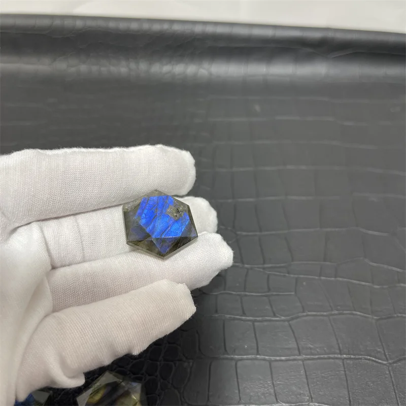 cristal-hexagonal-labradorite-naturelle-reflets-bleus Cristal hexagonal en labradorite naturelle avec des reflets bleus intenses, tenu par une main gantée.