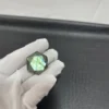 Cristal hexagonal en labradorite naturelle avec des reflets verts lumineux, tenu par une main gantée sur fond texturé noir.