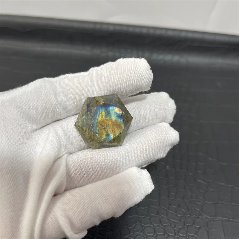cristal-hexagonal-labradorite-naturelle Cristal hexagonal en labradorite naturelle aux reflets bleu et or, tenu par une main gantée.