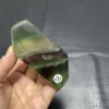 Cristal de quartz en fluorite naturelle avec des nuances de vert et de violet, tenu en main.