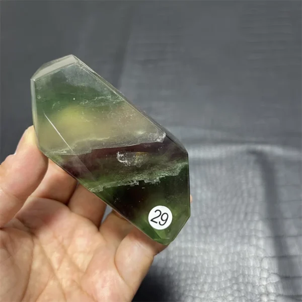 Cristal de quartz en fluorite naturelle avec des nuances de vert et de violet, tenu en main.
