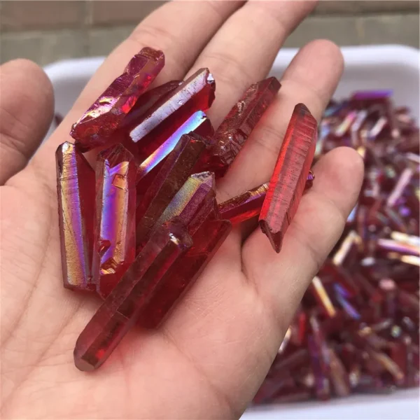 Gros plan de cristaux de quartz lémurien Aura Arc-en-Ciel Rouge iridescents tenus dans une main.