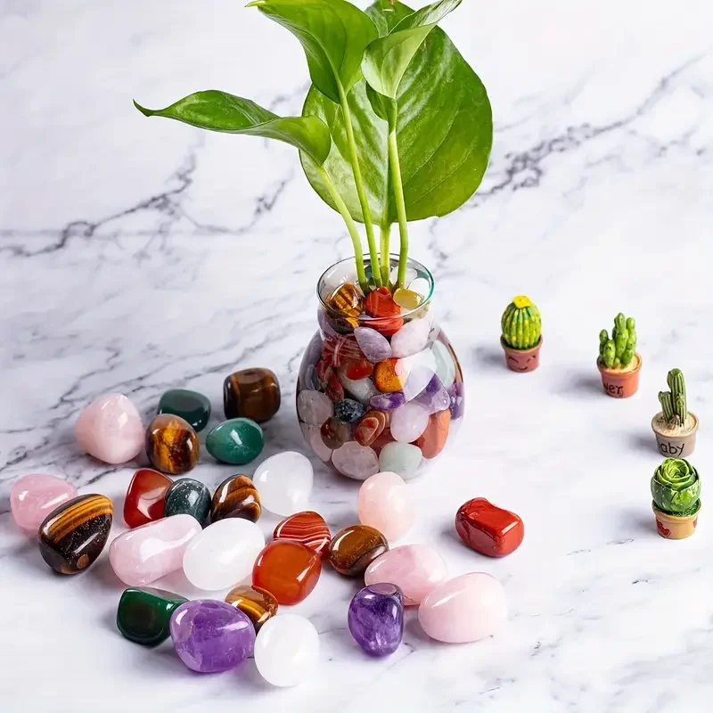 decor-plantes-pierres-cristal-polies-vase-multicolore Vase en verre rempli de pierres de cristal polies multicolores avec une plante verte, disposé sur un fond en marbre avec des mini cactus en décoration