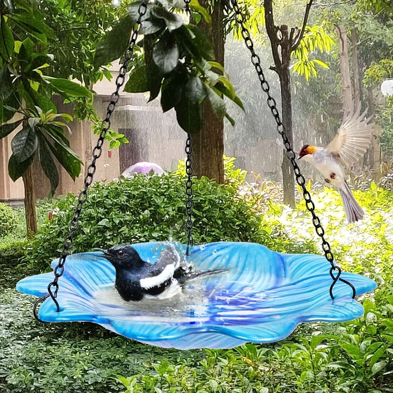 Mangeoire suspendue en forme de fleur bleue utilisée comme bain d'oiseaux, attirant les oiseaux dans un jardin.