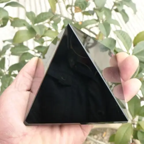 Pyramide en obsidienne noire, cristal de protection et guérison énergétique, tenue en main avec un arrière-plan de feuillage