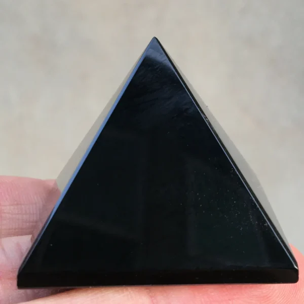 Pyramide en obsidienne noire, cristal de guérison et de protection énergétique, tenue entre les doigts sur fond neutre