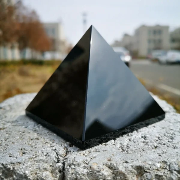 Pyramide de guérison en obsidienne noire, cristal de protection énergétique posé sur un rocher, avec un arrière-plan urbain flou