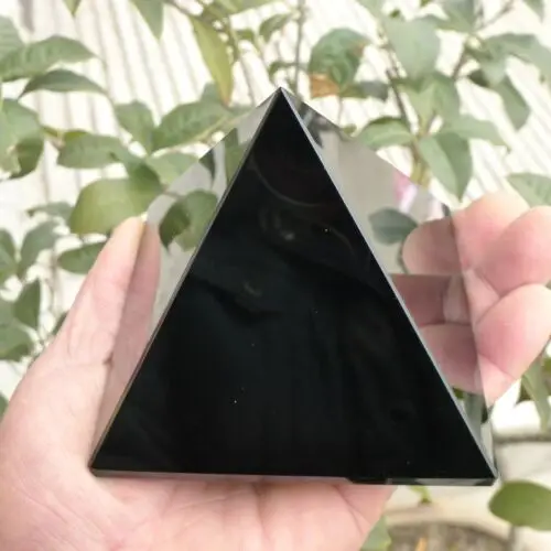 Pyramide de guérison en obsidienne noire, cristal de protection énergétique, tenue en main avec des plantes en arrière-plan