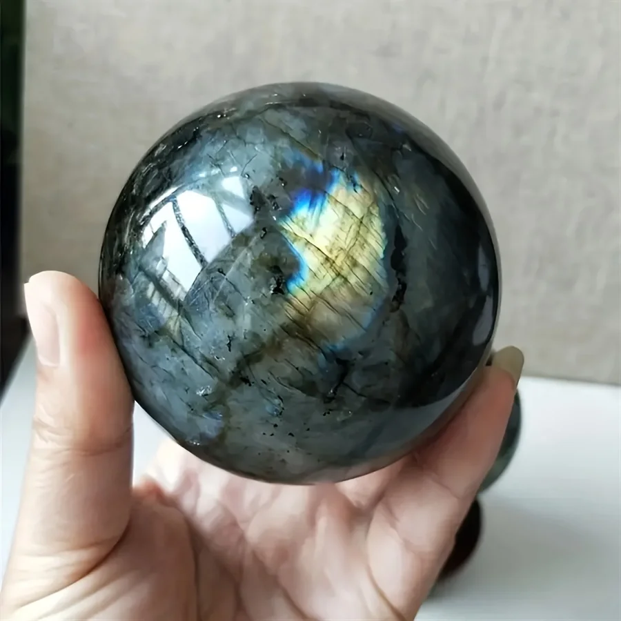 sphere-labradorite-naturelle-main-reflets Sphère de labradorite naturelle avec reflets bleus et dorés, tenue dans une main, idéale pour décoration et protection énergétique