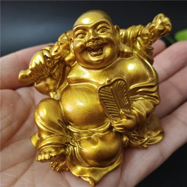 Statue de Bouddha Rieur Maitreya en résine dorée, petite taille, dans la main pour illustration.
