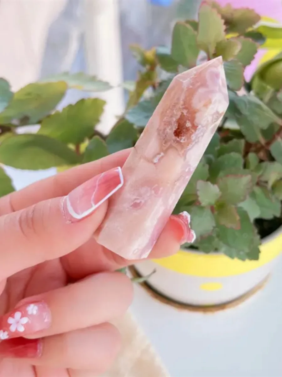 tour-quartz-rose-hermosa-sakura-agate-main-plante Tour de quartz rose Hermosa en Sakura Agate, cristal naturel tenu entre les doigts avec une plante en arrière-plan