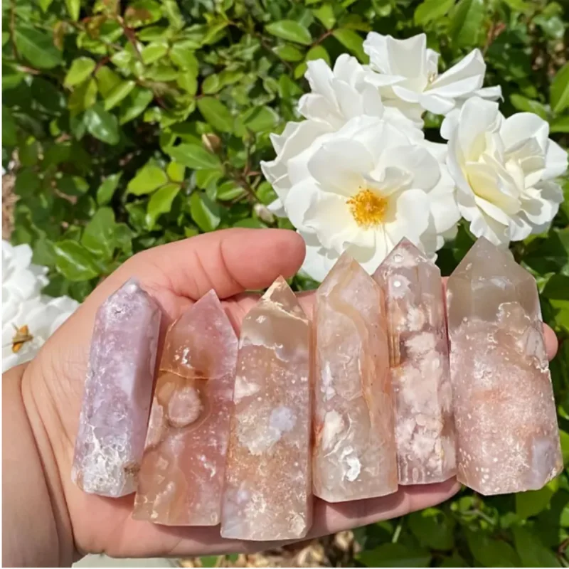 tours-quartz-rose-hermosa-sakura-agate-nature-fleurs Tours de quartz rose Hermosa en Sakura Agate, cristaux naturels tenus en main avec un arrière-plan de fleurs blanches